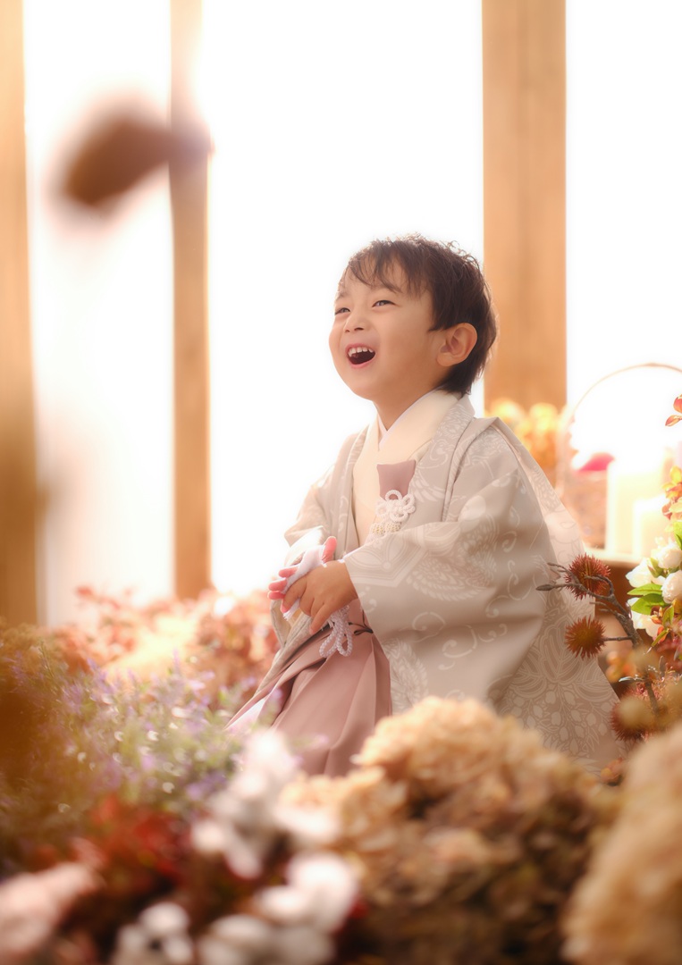 花に囲まれて声をあげて笑う生成りの羽織袴の男の子